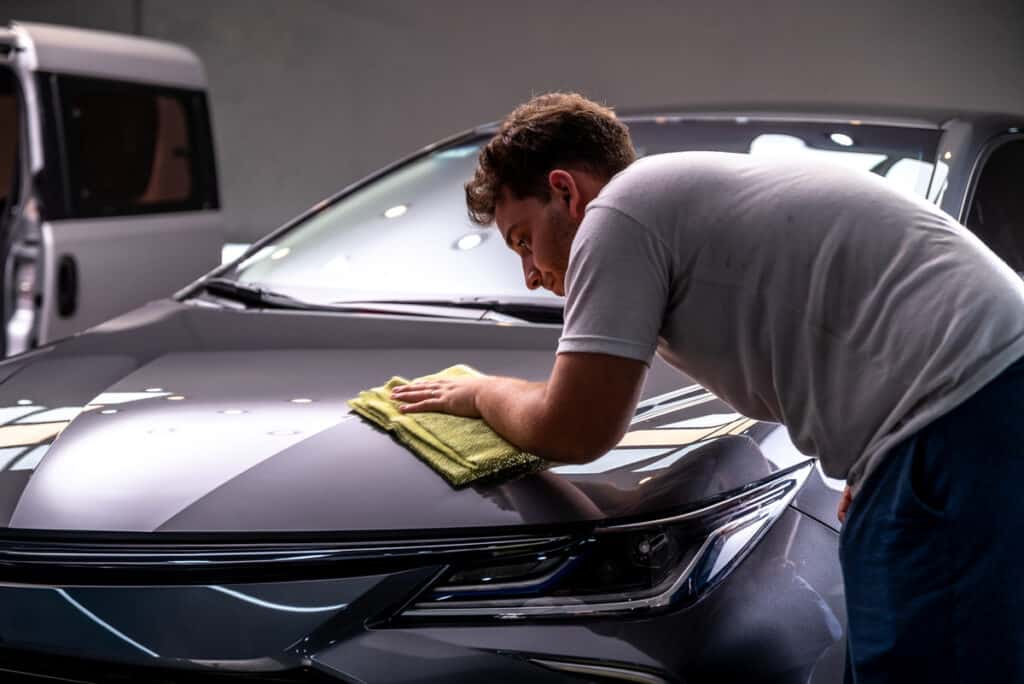 Homme polissant le capot d'une voiture sombre avec un chiffon microfibre jaune. Détailing automobile professionnel.