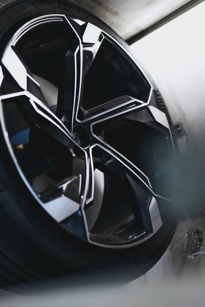 Jante de voiture noire et argentée au design complexe, pneu "POTENZA SPORT" visible. Surfaces brillantes en atelier automobile.