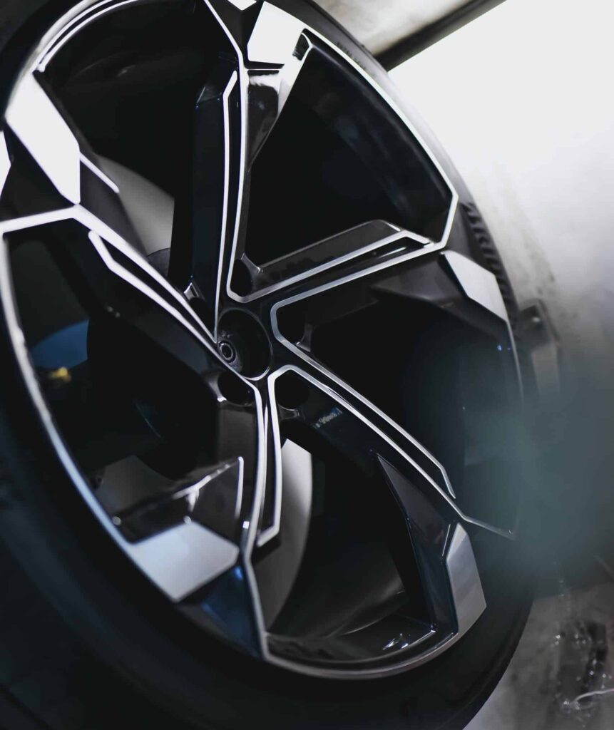 Jante de voiture noire et argentée au design complexe, pneu "POTENZA SPORT" visible. Surfaces brillantes en atelier automobile.